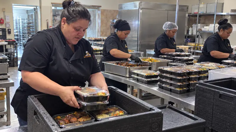 Deli-icious! Catering team packing plated meals in sealed containers into insulated carriers at a venue